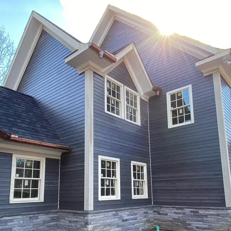 Ellis Builders Siding Contractor - dark blue fiber cement siding, white trim, and stone foundation on modern home