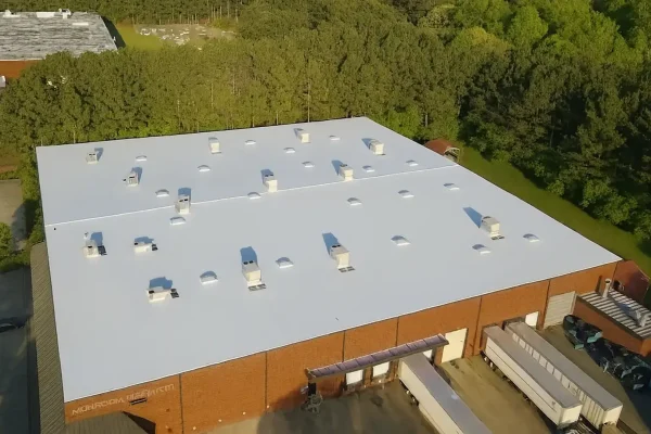 Commercial warehouse with new white flat roofing system surrounded by trees